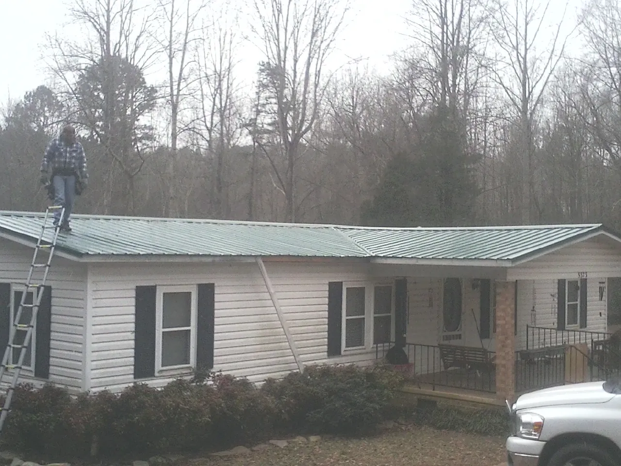 Worker on a ladder beside a new green metal roof on a ranch home in Petersburg