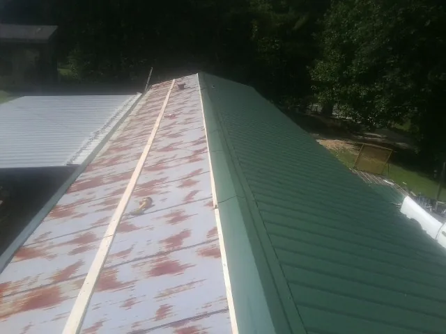 Old rusted panels beside newly installed green metal roofing — Wind Damage Roof Repair by Roofing Brothers in Petersburg